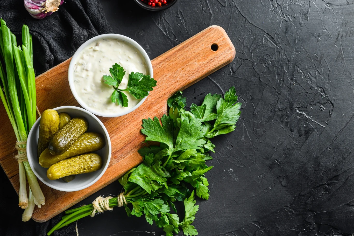 Spróbowalibyście gurken snack? Drewniana deska z miseczką sosu, marynowanymi ogórkami, zieloną cebulką i świeżą natką pietruszki.