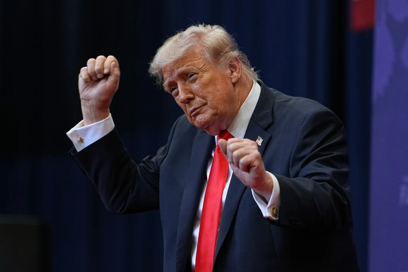 Populistyczna polityka Donalda Trumpa rozczarowała wielu Amerykanów. Gospodarz Białego Domu ma jednak powody do radości: europejscy przywódcy są znacznie mniej popularni Mężczyzna w garniturze z czerwonym krawatem unosi ręce w geście przypominającym taniec, stojąc na tle ciemnych, jednokolorowych zasłon.