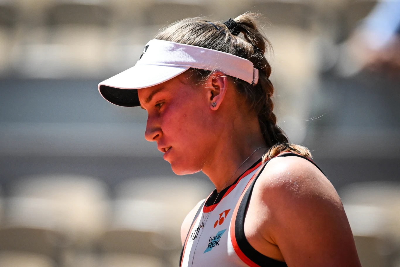 Jelena Rybakina Kobieta w sportowym stroju i białym daszku, z zaplecionym warkoczem, skupiona podczas meczu tenisowego.