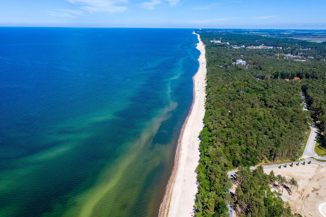 Urokliwa miejscowość nad Bałtykiem. Dlaczego warto odwiedzić Pobierowo? Szeroka plaża w Pobierowie, po lewej stronie Morze Bałtyckie, po prawej zielony las przy linii brzegowej.