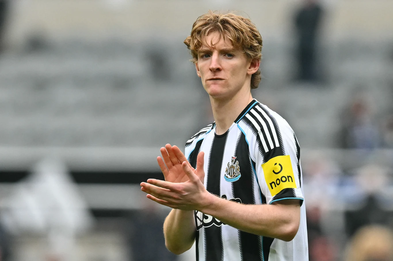 Piłkarz w pasiastym stroju drużyny Newcastle United z żółtą opaską na ramieniu klaszcze, spoglądając przed siebie na stadionie.