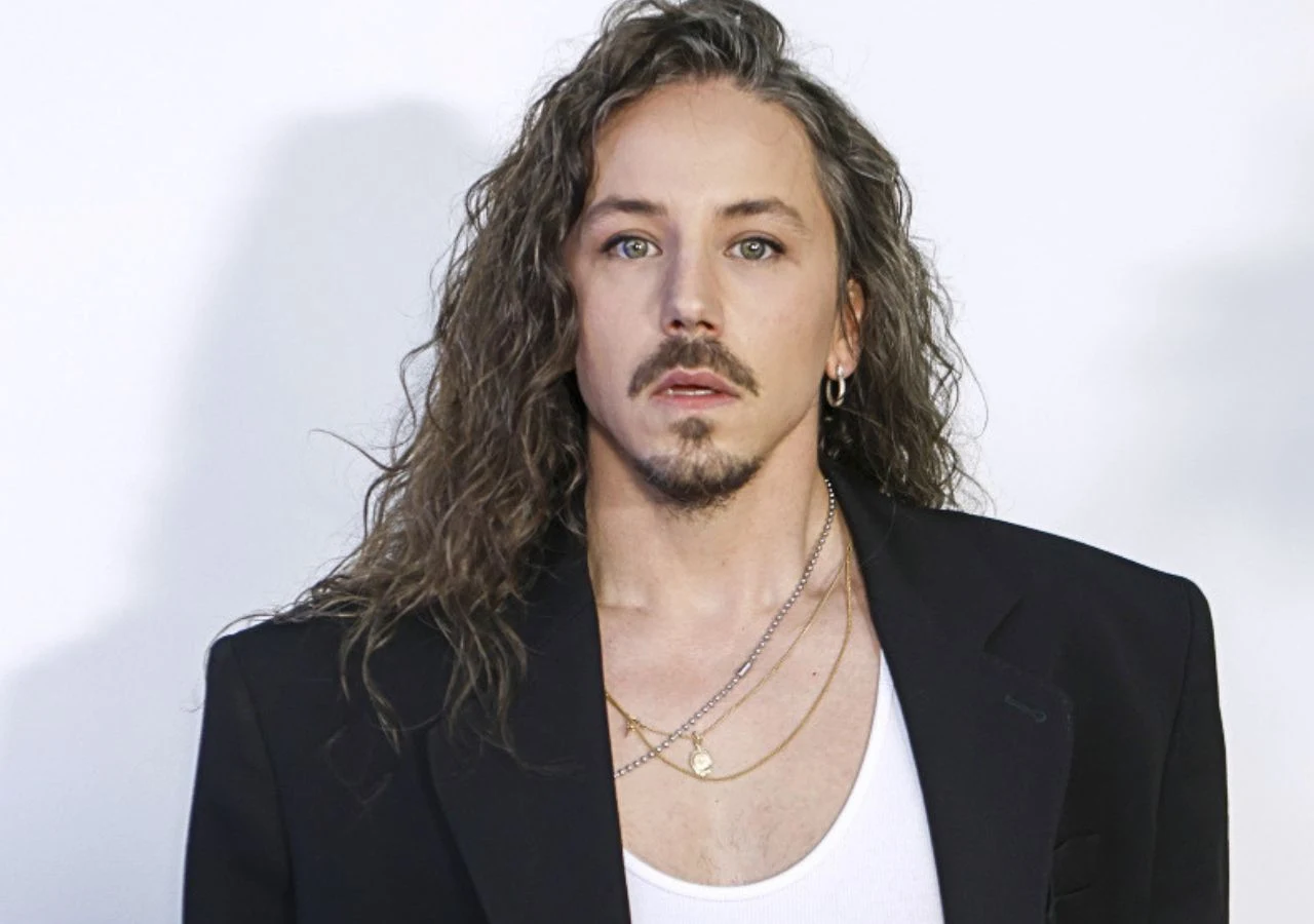 Michał Szpak Piosenkarz Michał Szpak w białej koszuli i czarnej marynarce. Ma przejęty wyraz twarzy.