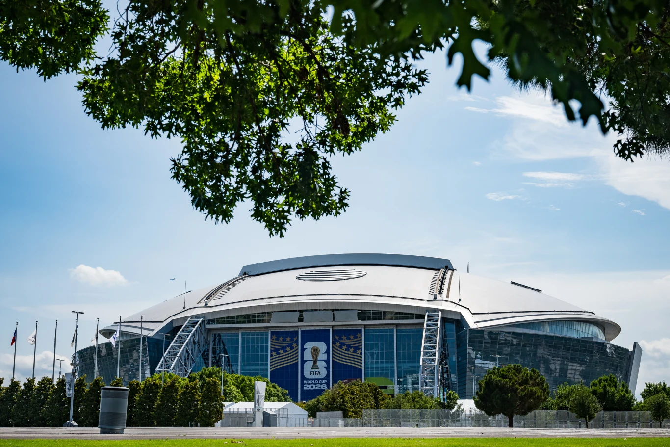 Piłkarskie MŚ 2026 odbędą się na najnowocześniejszych obiektach. AT&T Stadium w Arlington pomieści około 90 tys. widzów. AT&T Stadium w Arlington z zaokrąglonym dachem, szklanymi ścianami i logo MŚ 2026, otoczony zielenią.