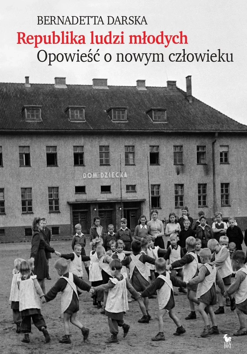 Okładka książki "Republika ludzi młodych. Opowieść o nowym człowieku" autorstwa Bernadetty Darskiej Grupa dzieci bawiących się w kręgu przed dużym, kilkupiętrowym budynkiem z napisem 'Dom Dziecka', obserwowana przez kilku dorosłych stojących w pobliżu wejścia.