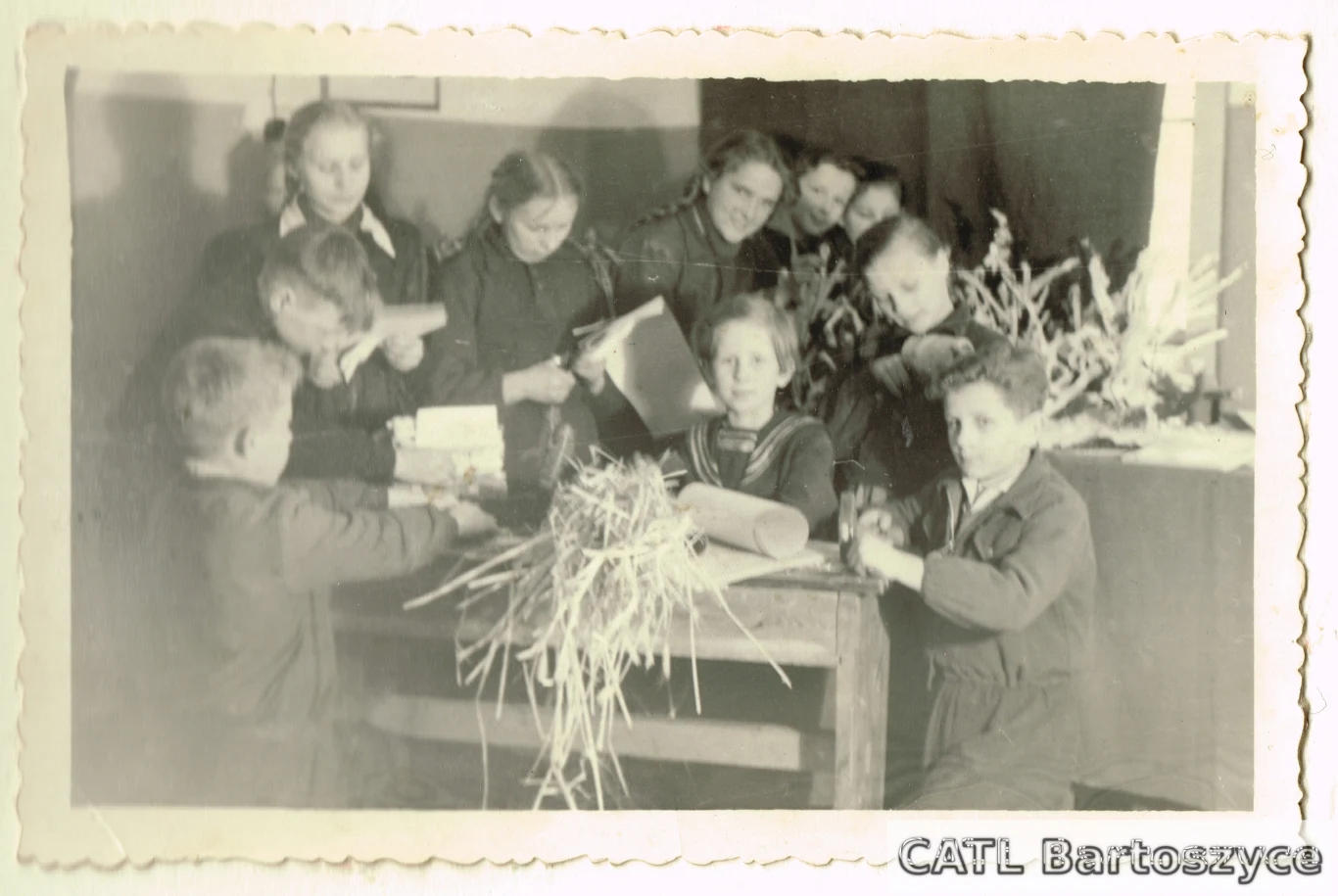 Dzieci podczas zajęć szkolnych, Bartoszyce, 1953 Grupa dzieci skupionych wokół stołu, na którym leży słoma oraz papierowe przedmioty, podczas wspólnej pracy manualnej.