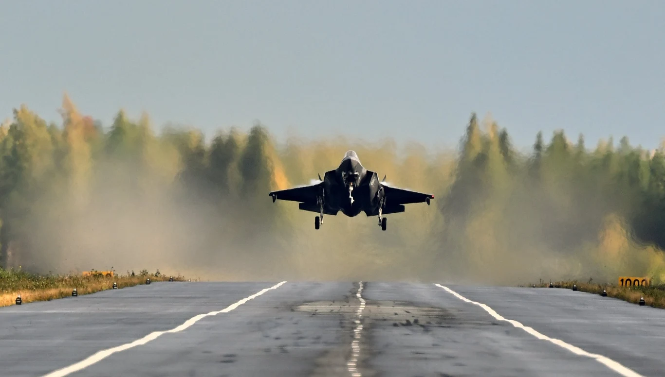 Norweski F-35 startujący z drogi podczas ćwiczeń w Finlandii Myśliwiec wojskowy momentalnie odrywający się od pasa startowego, unoszący się nad asfaltową powierzchnią na tle lasu.
