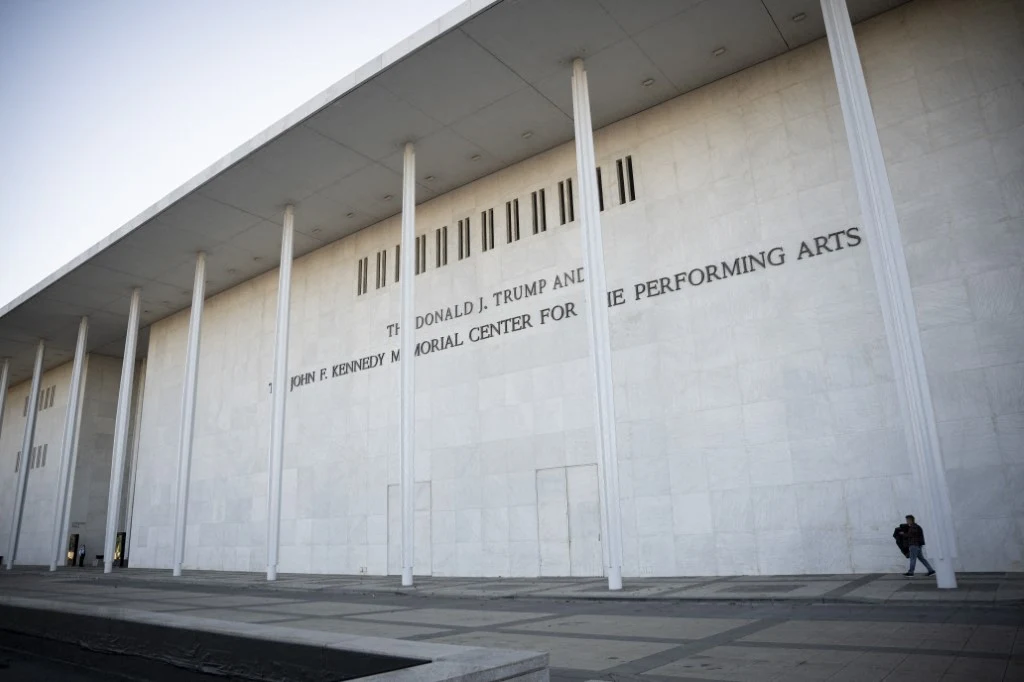 Biała fasada budynku John F. Kennedy Center for the Performing Arts ozdobiona wysokimi kolumnami, przy których na chodniku widoczna jest samotna postać.