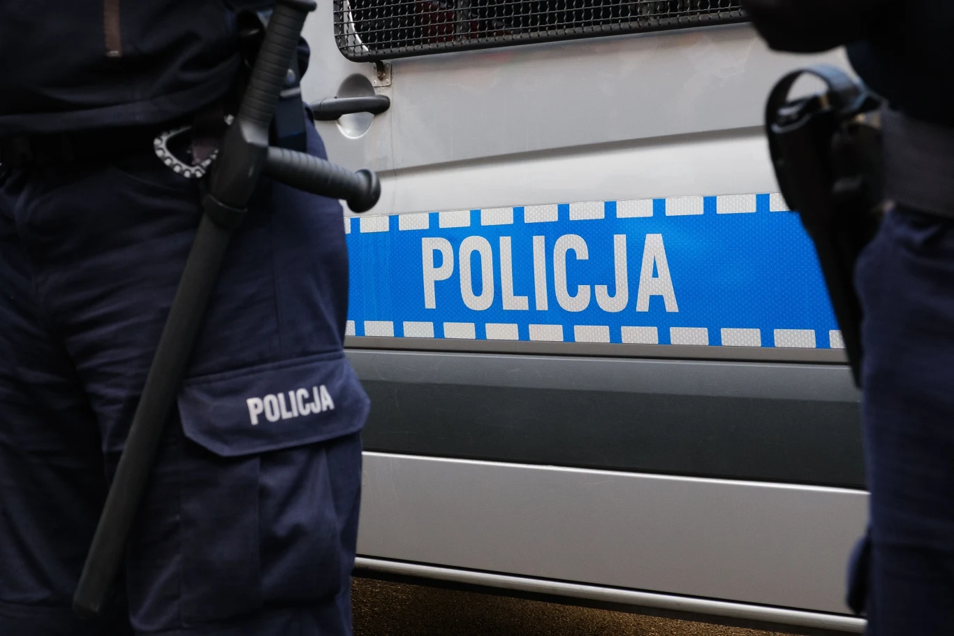 Kolejne zatrzymanie w związku z fałszywymi alarmami (zdj. ilustracyjne) Samochód policyjny, przed nim w kadrze widoczne nogi umundurowanych policjantów.