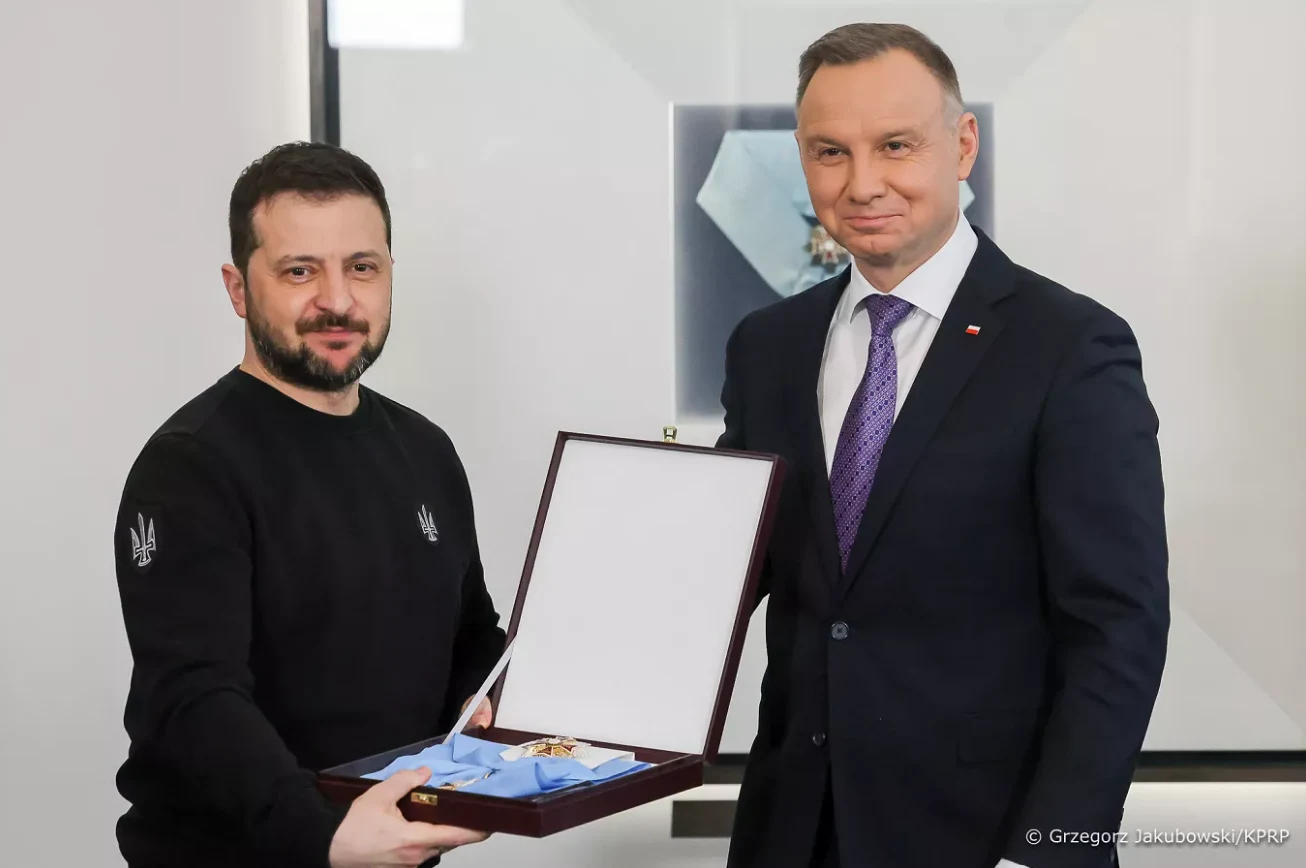 Dwóch mężczyzn stojących obok siebie, jeden z nich trzyma otwarte eleganckie etui z odznaczeniem umieszczonym w środku.