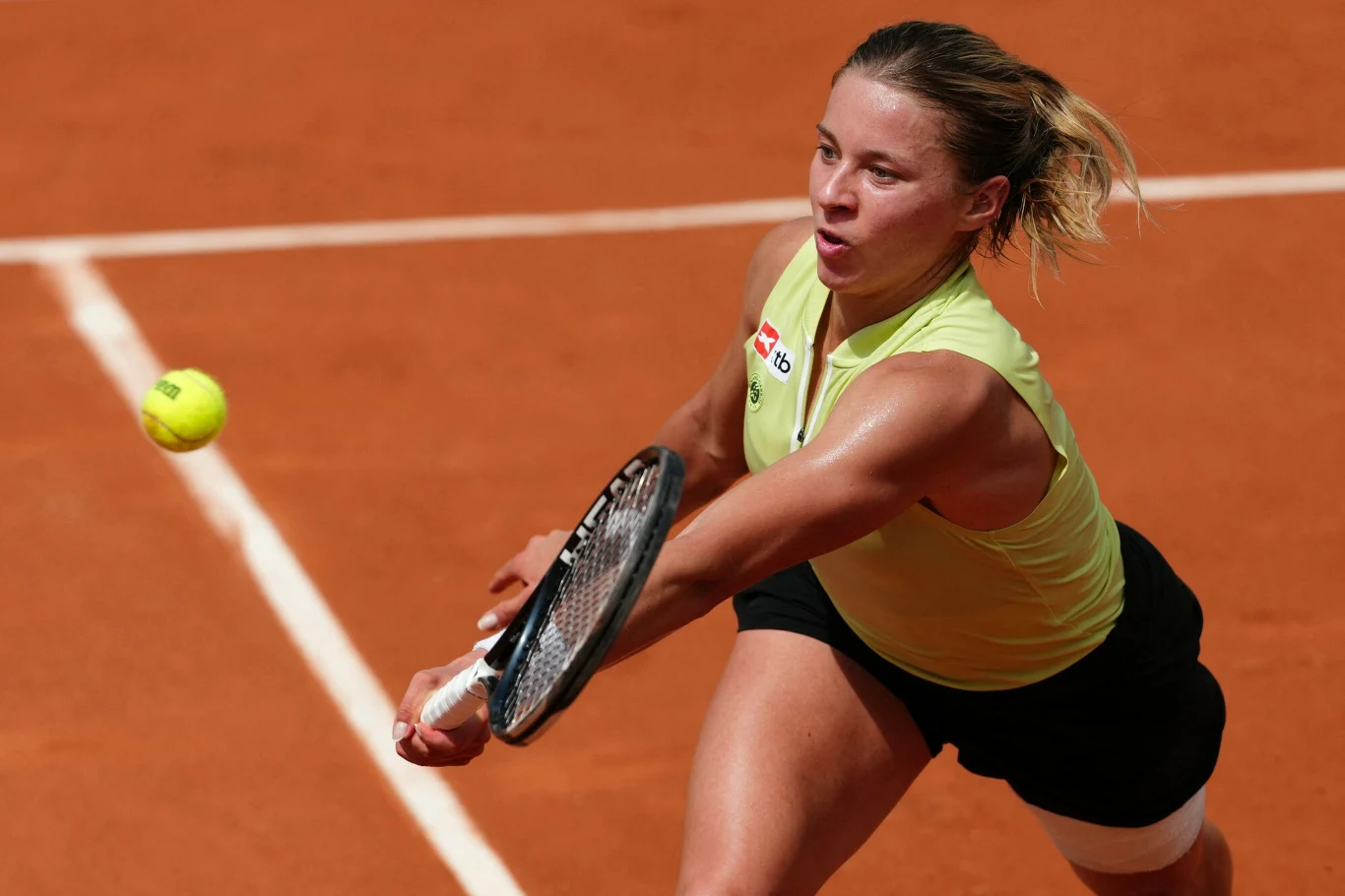 Kobieta w sportowym stroju odbijająca piłkę tenisową rakietą na kortach ziemnych podczas meczu.