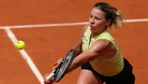 Kobieta w sportowym stroju odbijająca piłkę tenisową rakietą na kortach ziemnych podczas meczu.