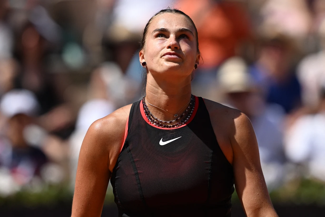 Kobieta w sportowym stroju z logo Nike na czarnej koszulce, patrzy w górę z poważnym wyrazem twarzy, w tle rozmyta publiczność na trybunach.