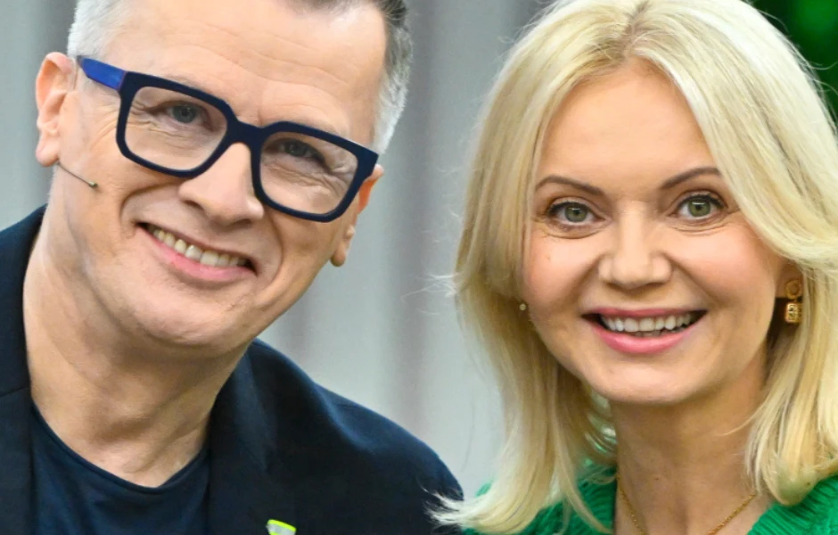 Wojciech Majchrzak i Olga Borys Uśmiechnięta kobieta z blond włosami w zielonym swetrze oraz mężczyzna w okularach i granatowej marynarce stoją obok siebie, tworząc pogodną, przyjazną atmosferę.