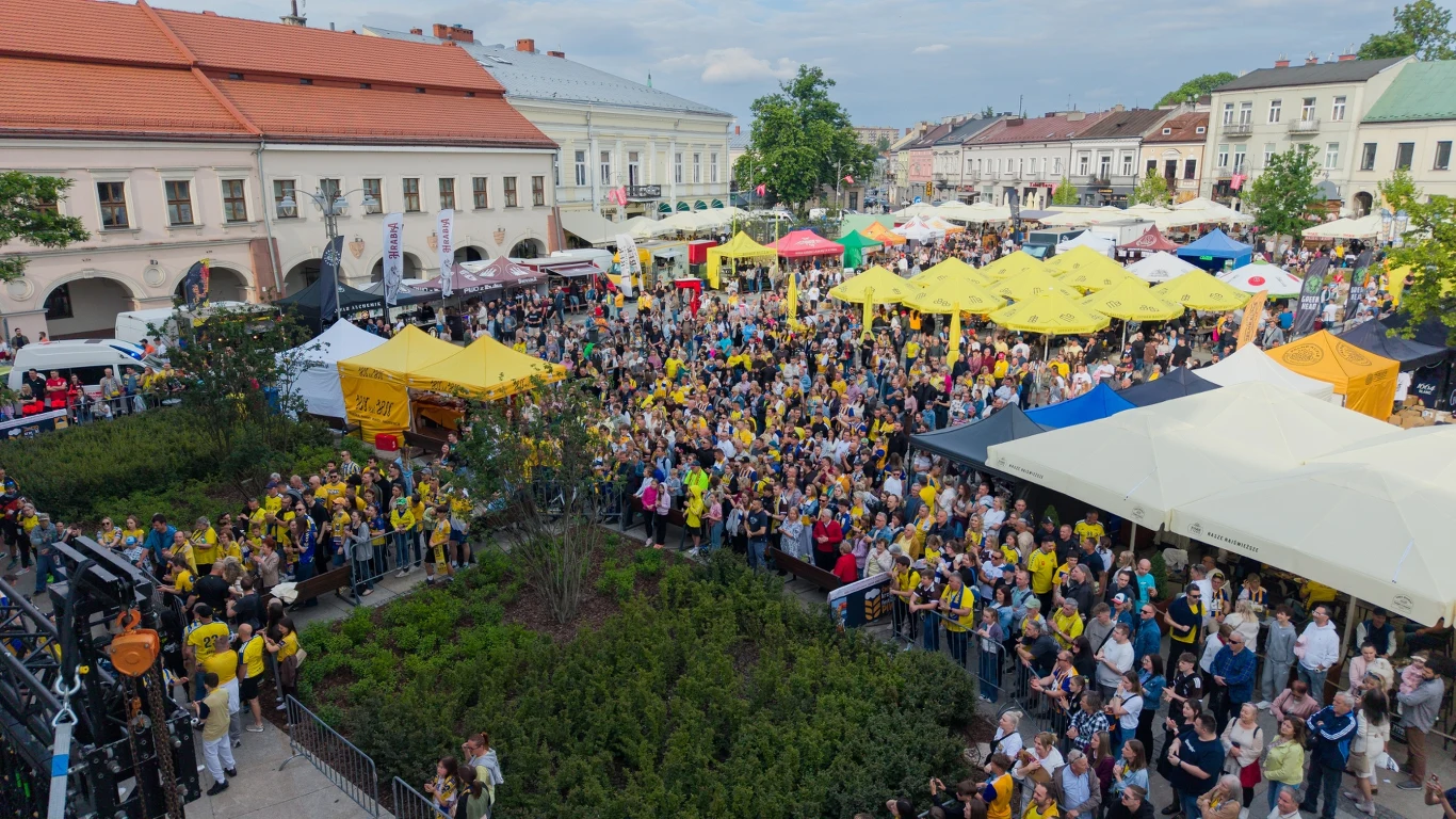 Duża grupa ludzi zgromadzona na rynku miejskim podczas plenerowego wydarzenia, liczne kolorowe namioty, transparenty i zabytkowe kamienice w tle.