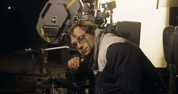 Mężczyzna w okularach opiera głowę o profesjonalną kamerę filmową, skupiony na pracy podczas nagrania w studiu oświetlonym jasnym światłem.
