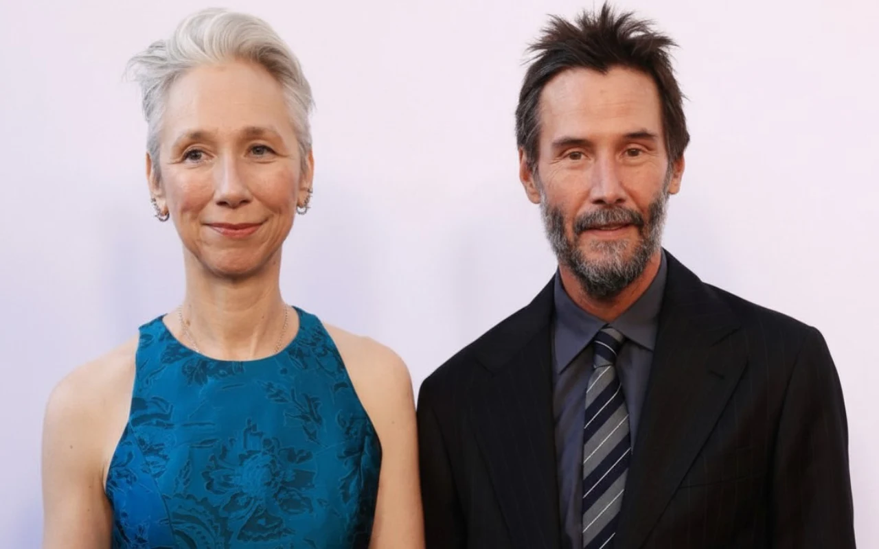 Alexandra Grant i Keanu Reeves Alexandra Grant w niebieskiej sukni bez rękawów i Keanu Reeves w ciemnym garniturze na jasnym tle.