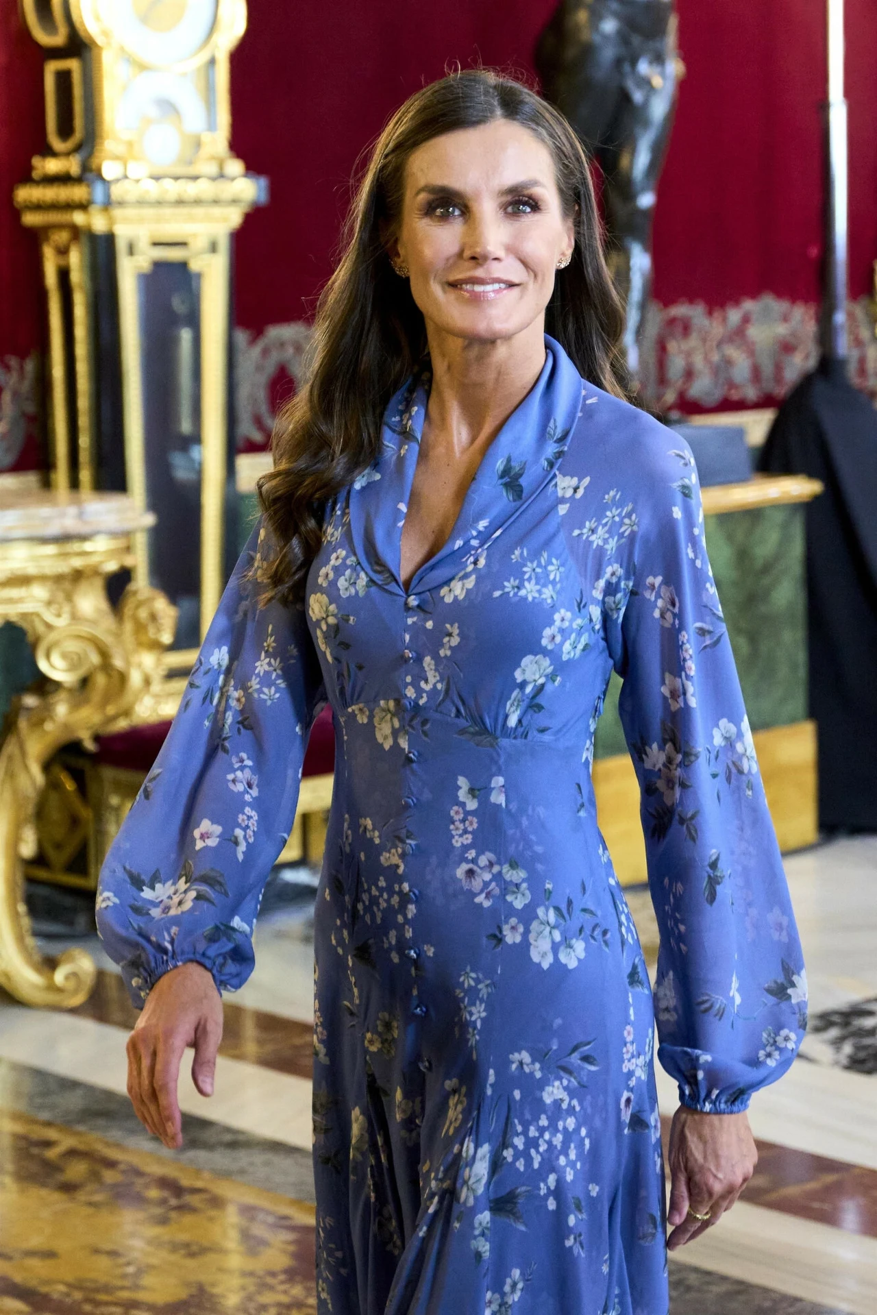 Sukienkę projektu Juana Vidala królowa Letizia miała na sobie już podczas obchodów Dnia Narodowego w Pałacu Królewskim 12 października 2023 roku Kobieta w długiej, niebieskiej sukience w kwiaty stoi w bogato zdobionym wnętrzu ze złotymi i czerwonymi elementami dekoracyjnymi.