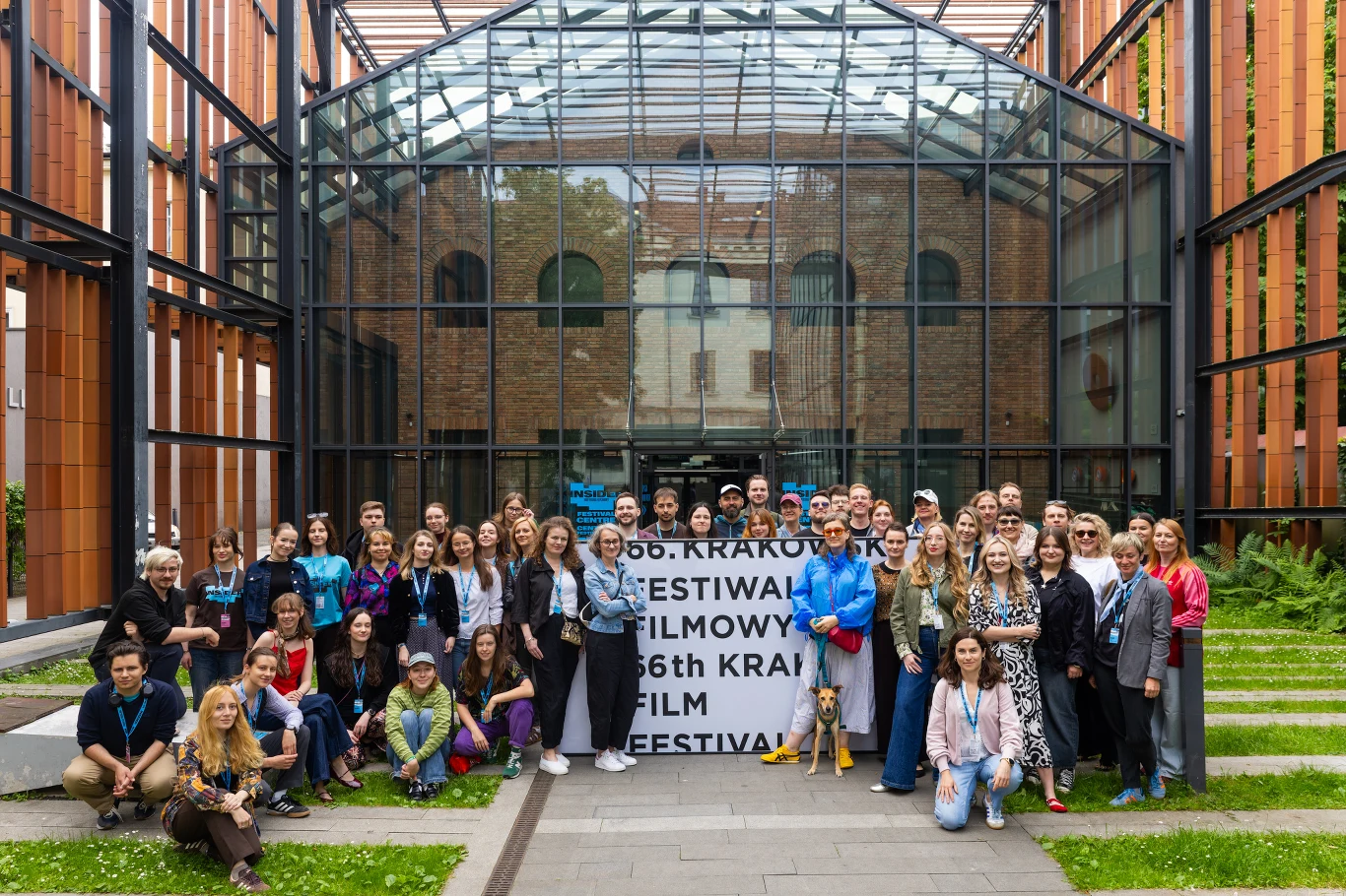 Ekipa organizująca Krakowski Festiwal Filmowy 2026 Grupa uczestników zgromadzona przed wejściem do przeszklonego budynku festiwalowego, w tle widoczny baner informujący o 66. Krakowskim Festiwalu Filmowym.