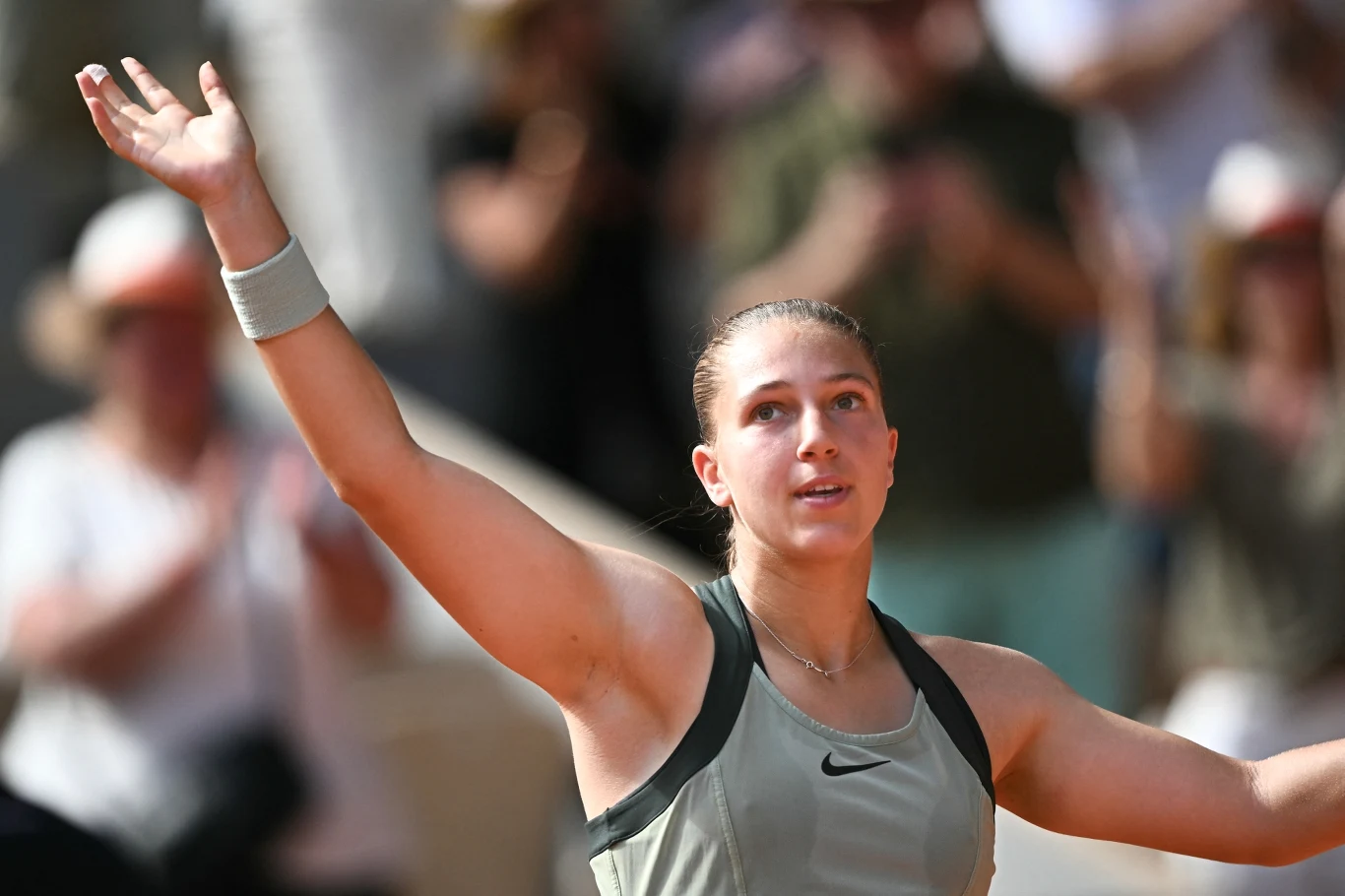 Tenisistka w sportowym stroju z podniesionymi ramionami, z wyrazem radości na twarzy, na tle rozmytej, klaskającej publiczności.