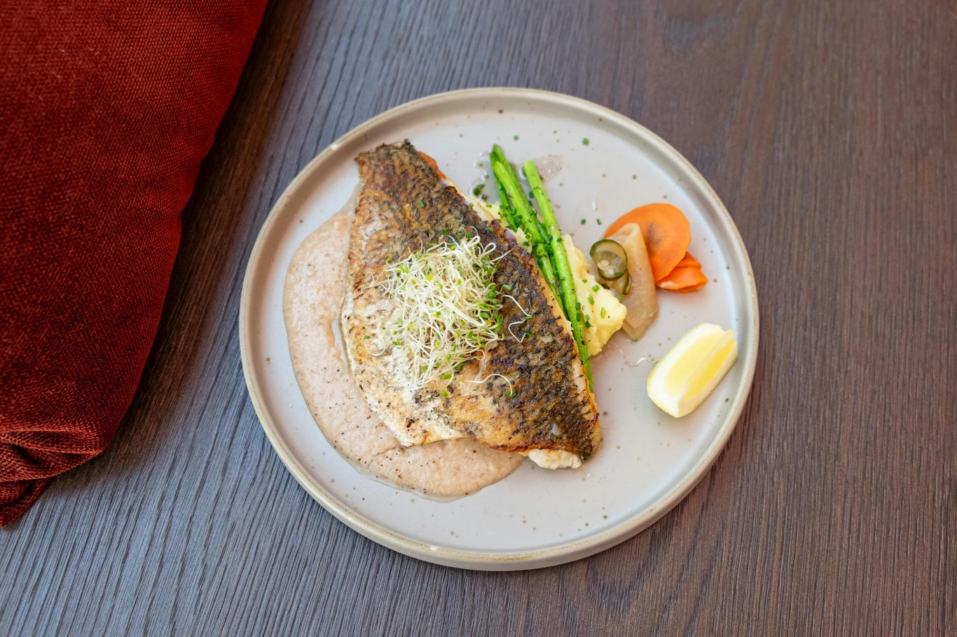 Pieczona dorada to posiłek doskonały w lekkiej diecie seniora Grillowany filet dorady na kremowym sosie z zielonymi szparagami, kiełkami, marchewką i cytryną na talerzu.