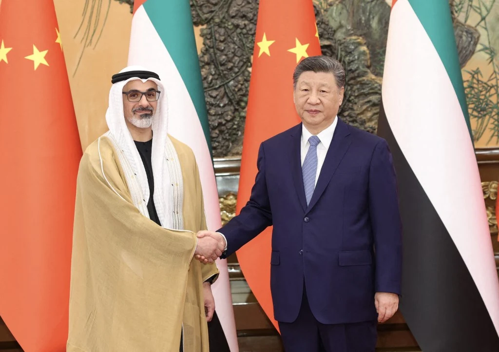 Chalid bin Mohamed bin Zajid al-Nahjan i Xi Jinping, 14 kwietnia 2026 r. Dwóch mężczyzn w oficjalnych strojach podaje sobie ręce na tle flag Chin i Zjednoczonych Emiratów Arabskich.