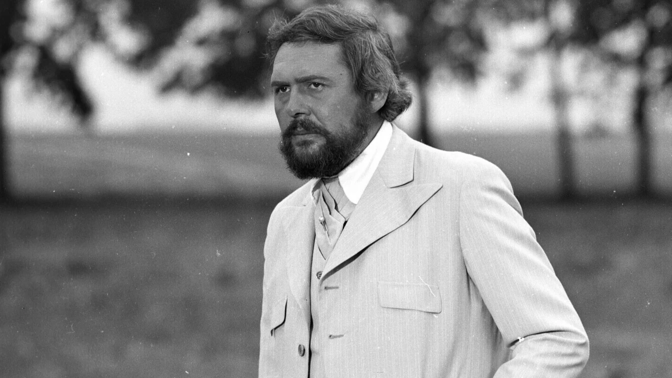 Kadr z filmu "Noce i dnie" Mężczyzna z brodą w jasnym garniturze i kamizelce na tle rozmytych drzew, kadr z filmu "Noce i dnie".