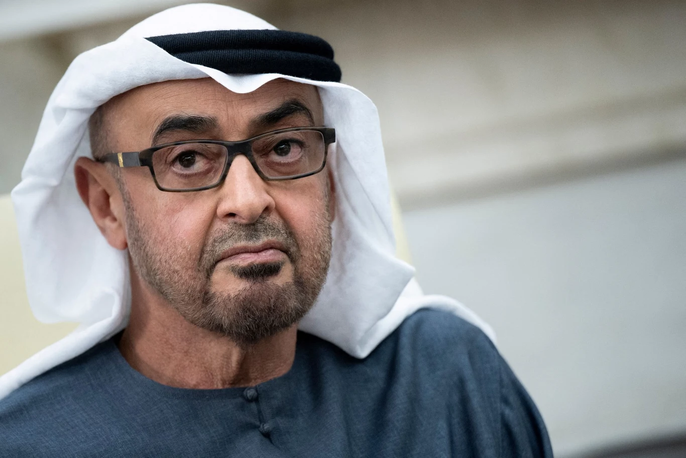 Prezydent ZEA Muhammad ibn Zajid Al Nahajjan Mężczyzna w okularach i tradycyjnym arabskim stroju, składającym się z białej kefiji i ciemnej tuniki, z poważnym wyrazem twarzy.