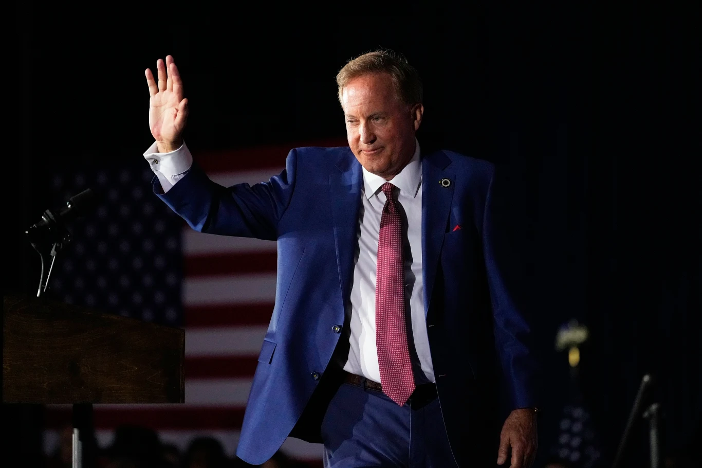 Ken Paxton dzięki Donaldowi Trumpowi wygrał republikańskie prawybory w Teksasie. Demokraci wierzą, że są w stanie go pokonać Mężczyzna w granatowym garniturze i czerwonym krawacie unosi rękę w geście powitania, w tle widoczna flaga Stanów Zjednoczonych.