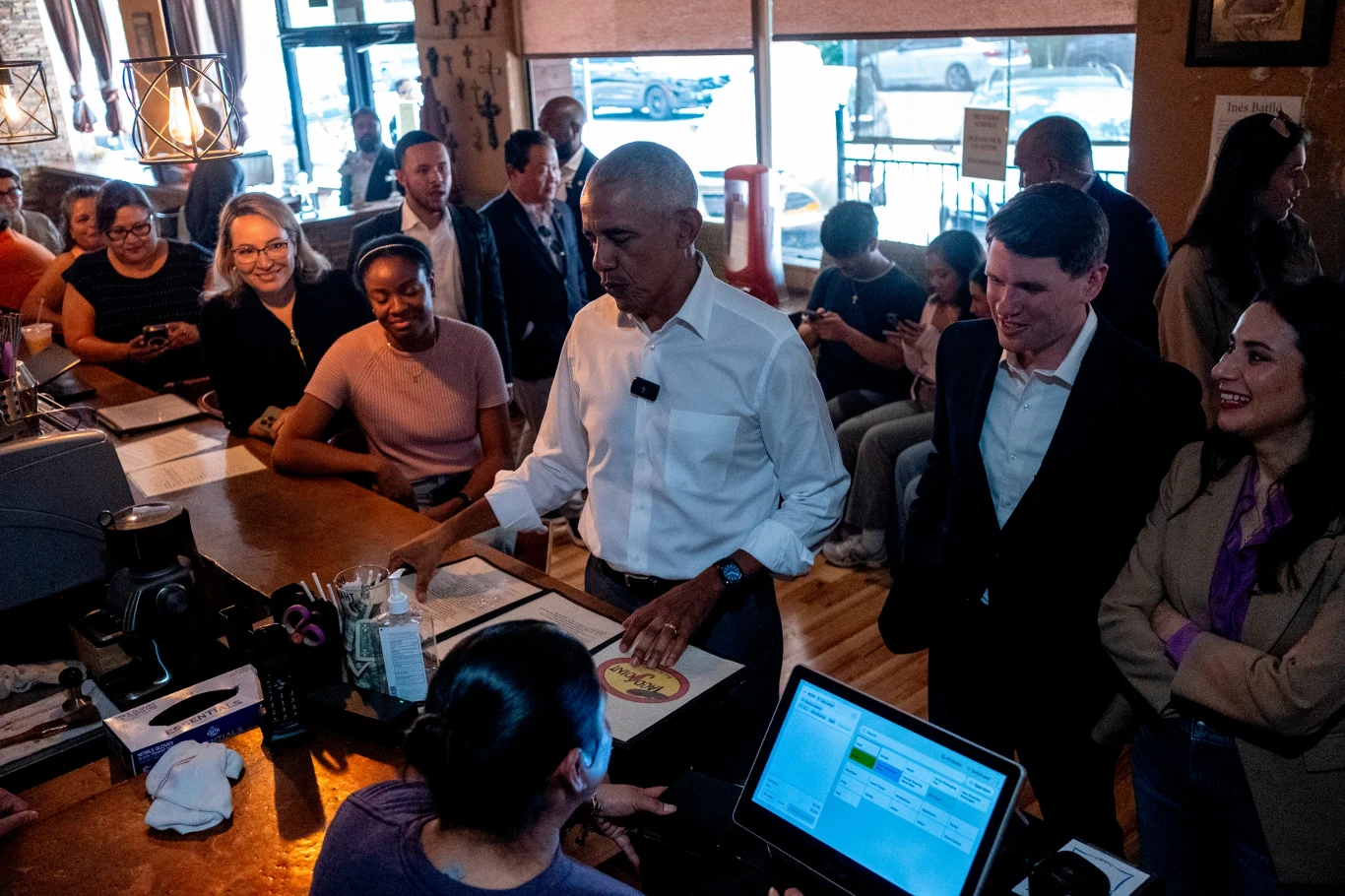 W kampanię wyborczą Talarico włączył się Barack Obama Mężczyzna w białej koszuli z mikrofonem przypiętym do kołnierza stoi przy ladzie kawiarni, trzymając w ręku talerz z jedzeniem, otoczony przez uśmiechniętych ludzi i personel, przy kasie oraz w tle, w klimatycznym wnętrzu kawiarni.