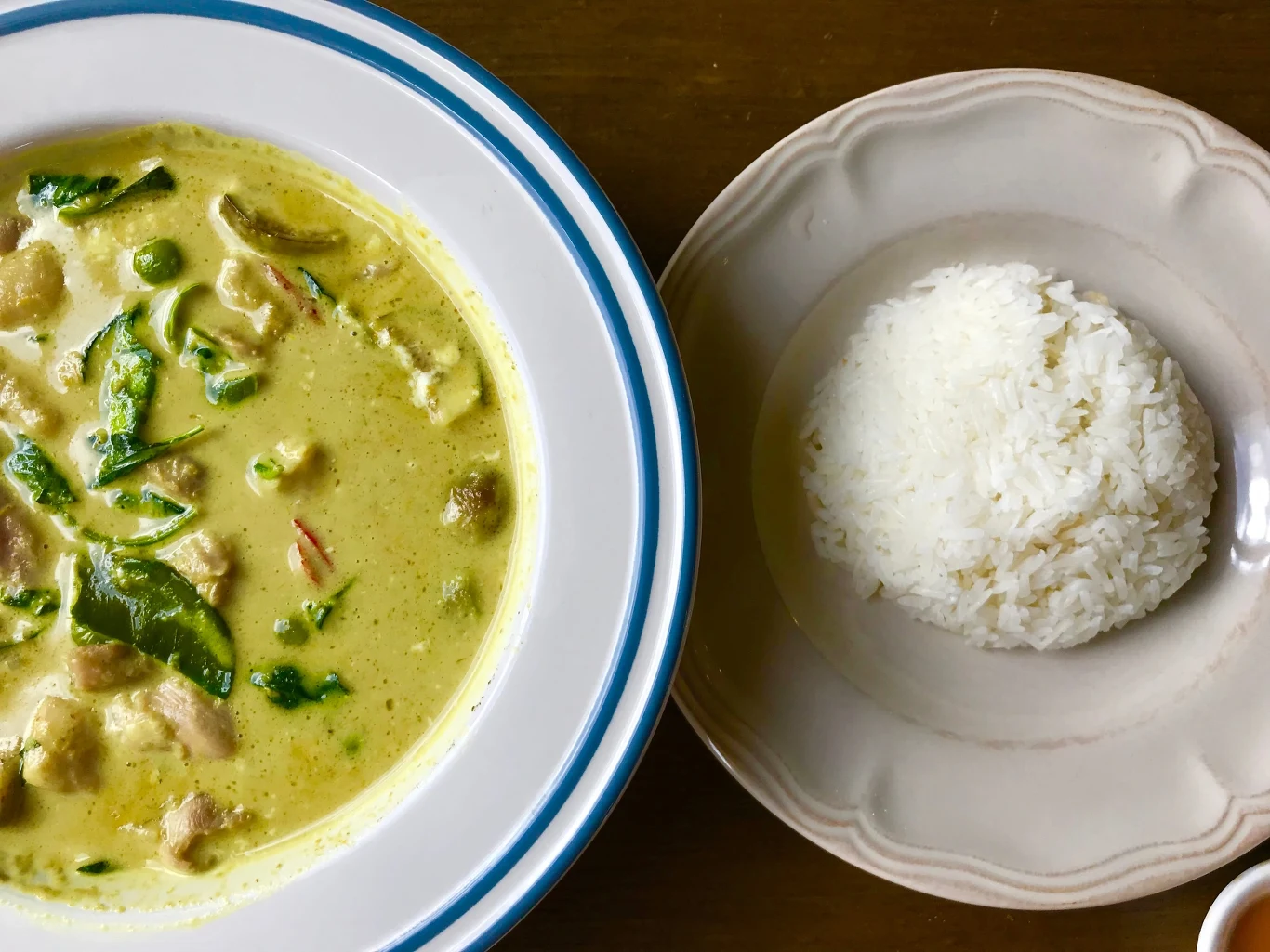 Porcja jasnego curry z kawałkami mięsa, groszkiem i liśćmi, podana obok kopca białego ryżu na oddzielnym talerzu.