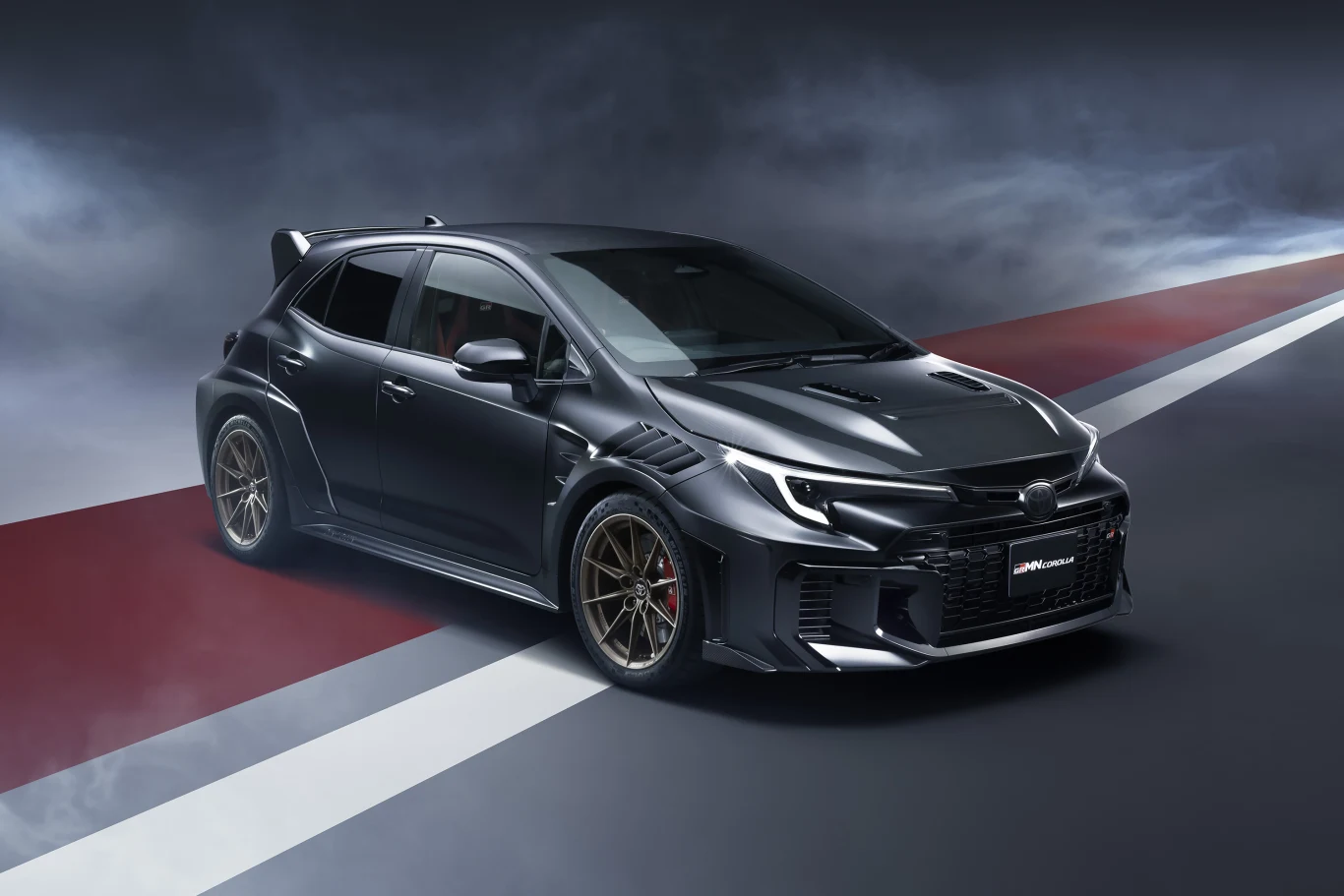 Czarny sportowy hatchback o agresywnej stylistyce nadwozia, szerokich nadkolach, dużych felgach i nisko osadzonym spojlerze na torze z efektownym oświetleniem i dynamiczną perspektywą.