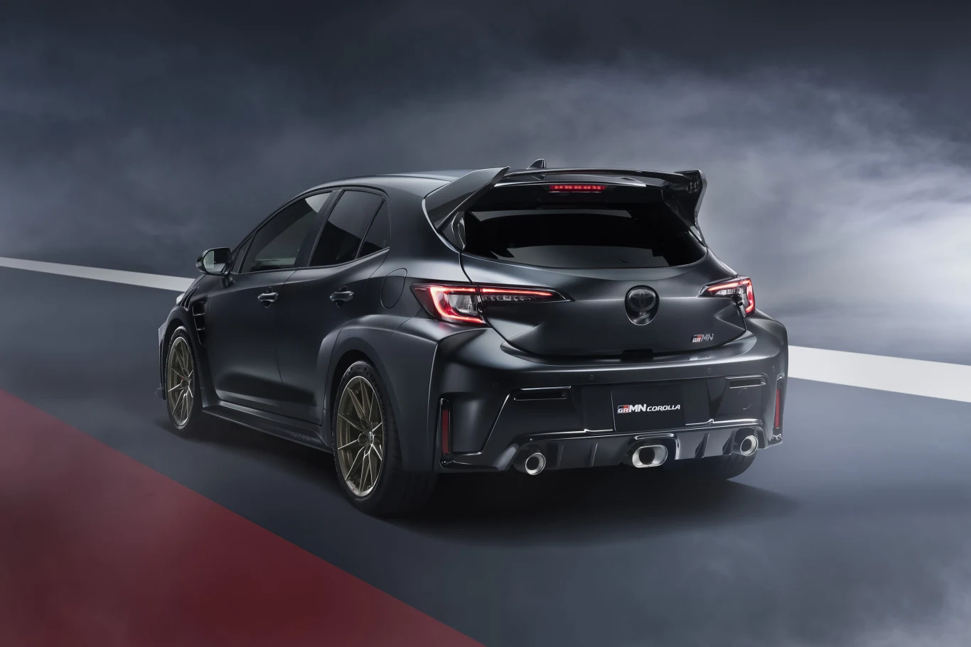 Czarny hot-hatch z agresywnymi liniami nadwozia, dużym tylnym spojlerem, podwójnymi końcówkami wydechu oraz sportowymi felgami, ustawiony na asfaltowej nawierzchni.