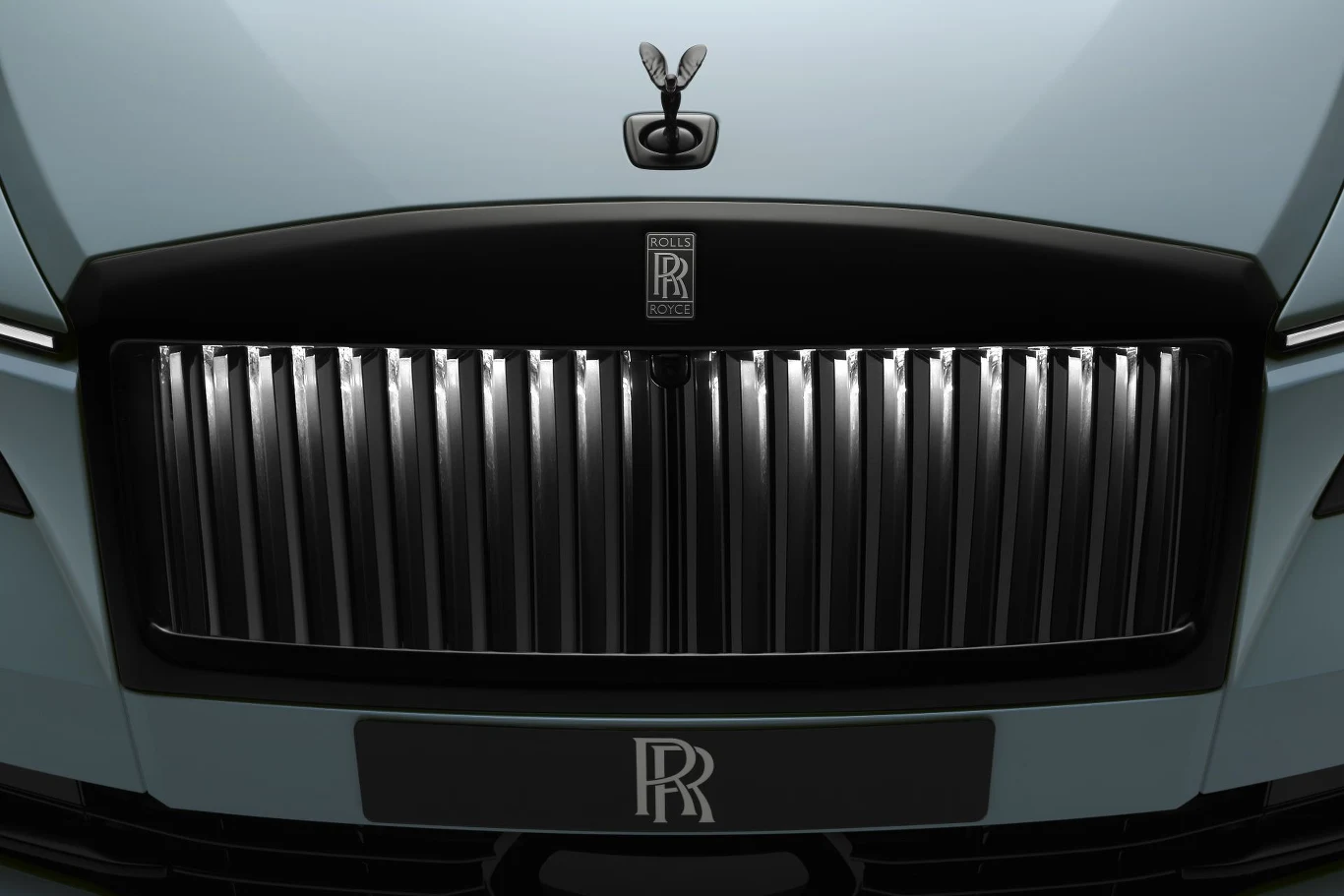 Chromowana atrapa chłodnicy z pionowymi żebrami, czarne logo Rolls-Royce oraz charakterystyczna figurka Spirit of Ecstasy na masce samochodu.