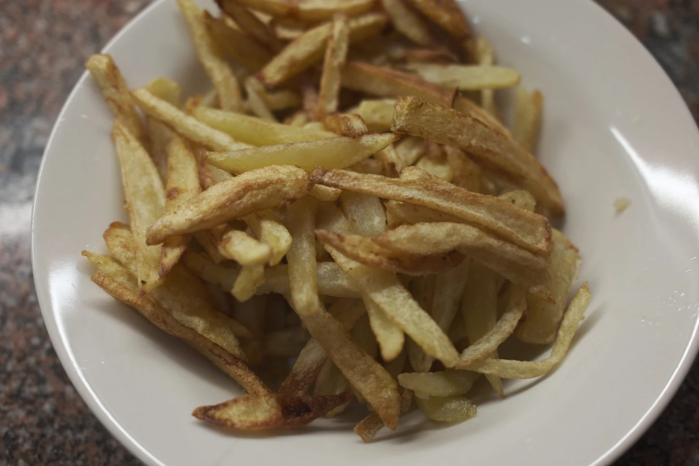 French fries in a white plate on the kitchen table. Selective focus. Frytki na białym talerzu, na stole kuchennym, widok z góry.