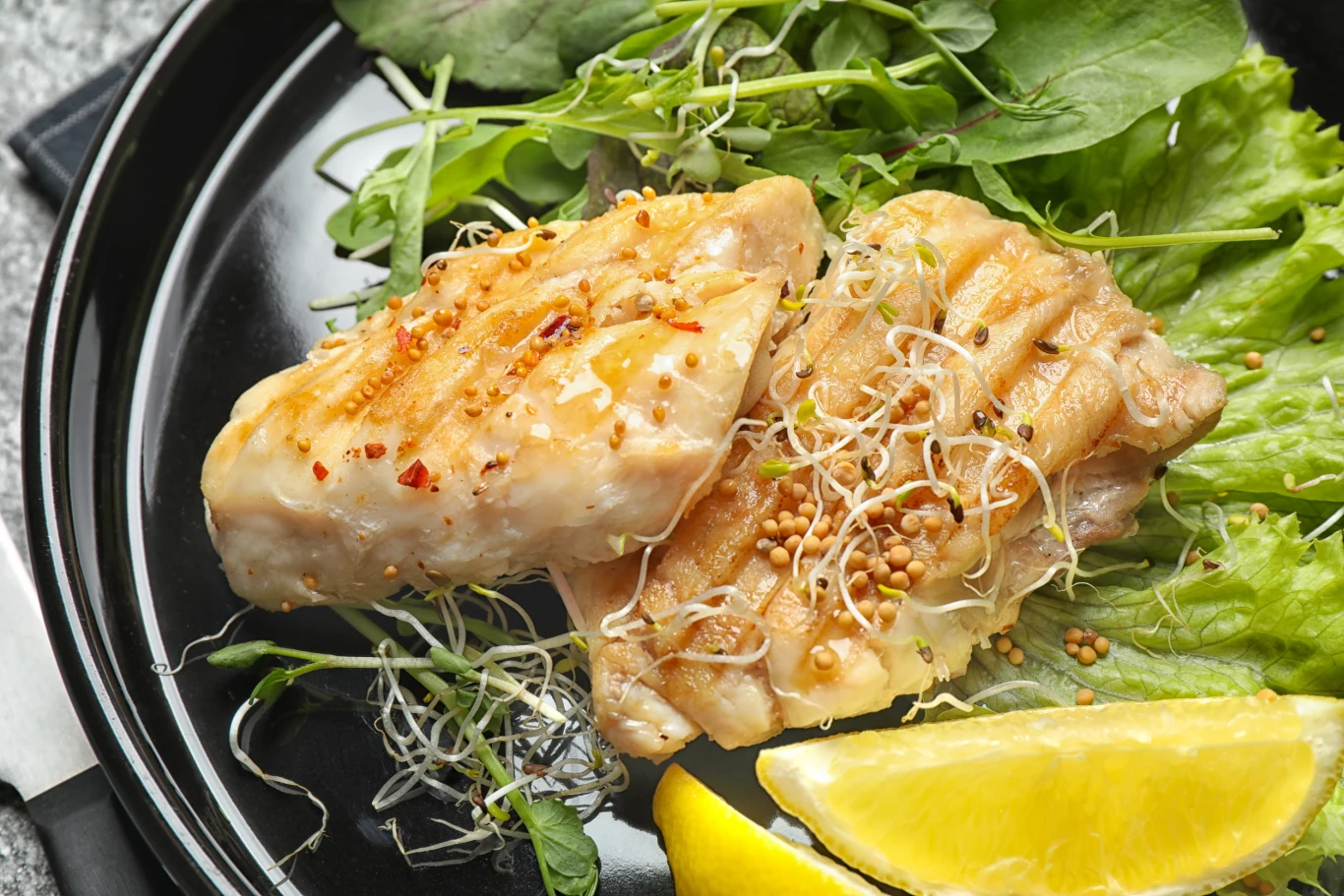 Sandacz odmieni grillowe menu Dwa kawałki grillowanej ryby posypane kiełkami i ziarnami gorczycy, podane na liściach sałaty z plasterkiem cytryny.