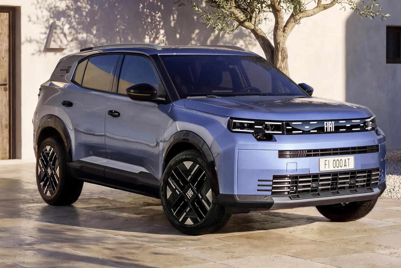 Niebieski SUV marki Fiat zaparkowany na jasnym podjeździe, w tle ściana budynku i drzewo oliwne.