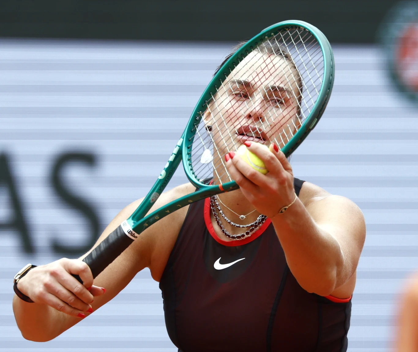 Zawodniczka tenisowa w ciemnym stroju sportowym podczas serwisu z piłką przy rakiecie na tle kortu.