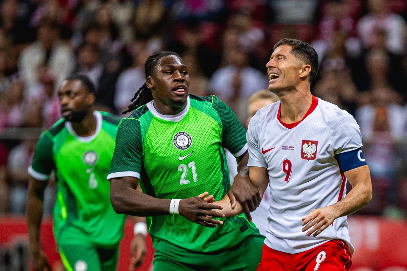Robert Lewandowski (z prawej) Robert Lewandowski i piłkarz Nigerii rywalizują o piłkę podczas meczu, biały i zielony strój sportowy.