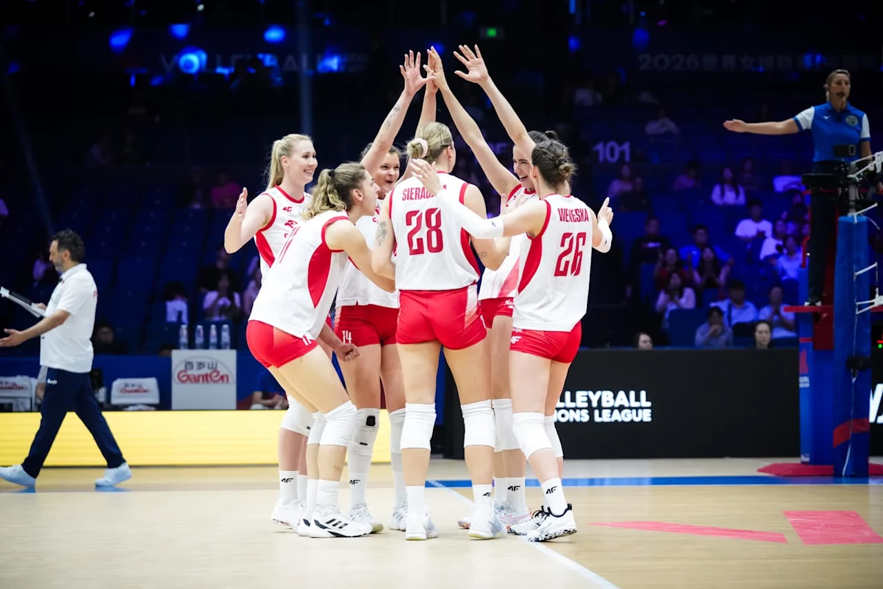 Grupa siatkarek w biało-czerwonych strojach świętuje zdobycie punktu, unosząc dłonie do góry i stojąc w ścisłym kręgu na boisku podczas meczu.