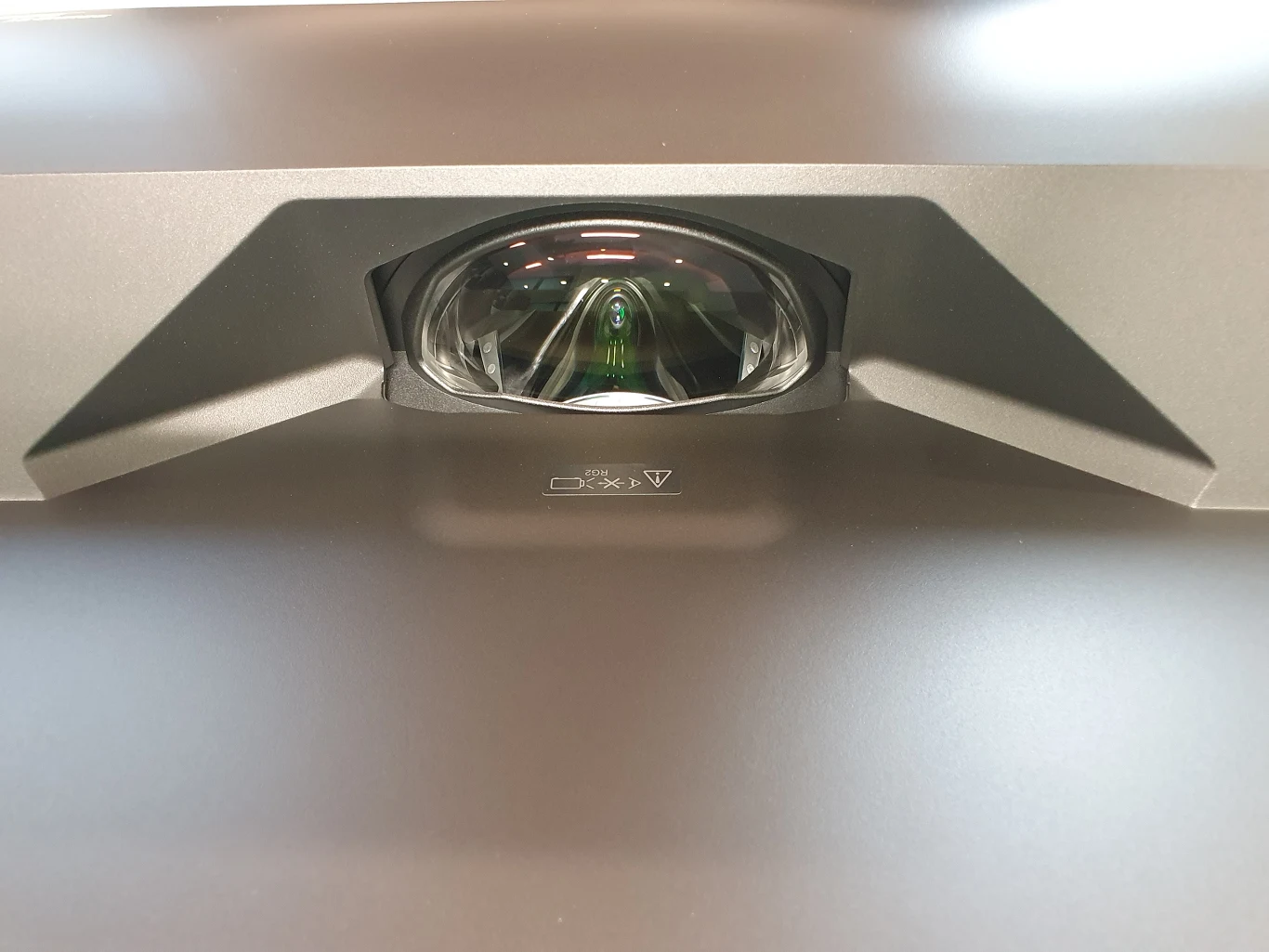 Lifestudio Grand EH-LS670 Centralnie umieszczony projektor ultrakrótkoogniskowy z dużą soczewką i wyraźnym panelem ochronnym wokół niej.