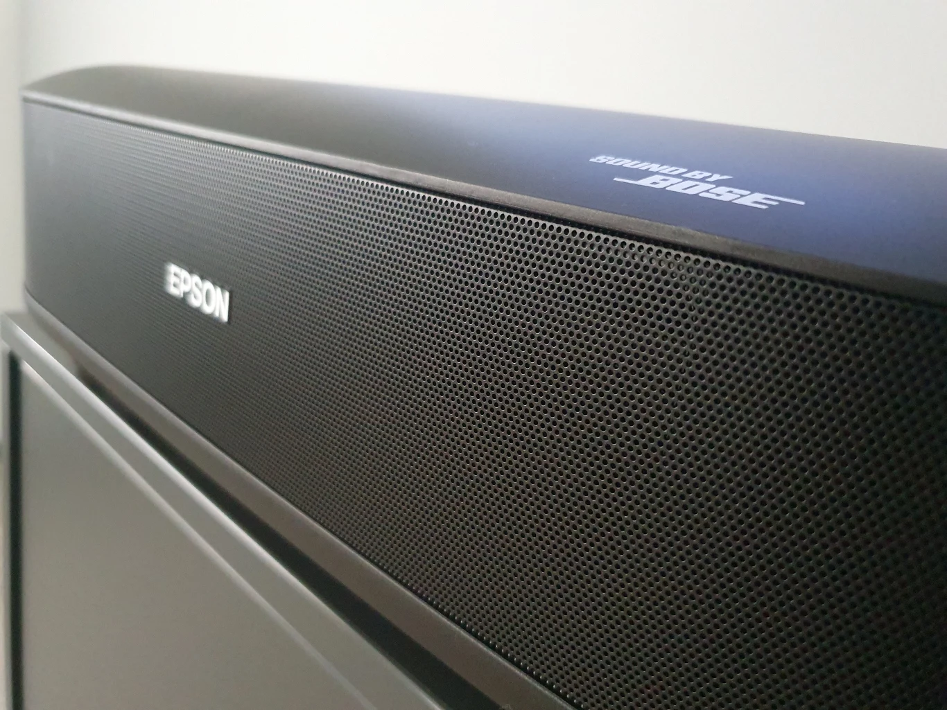 Lifestudio Grand EH-LS670 Czarna listwa dźwiękowa z logo Epson oraz napisem 'Powered by Bose', umieszczona nad telewizorem.