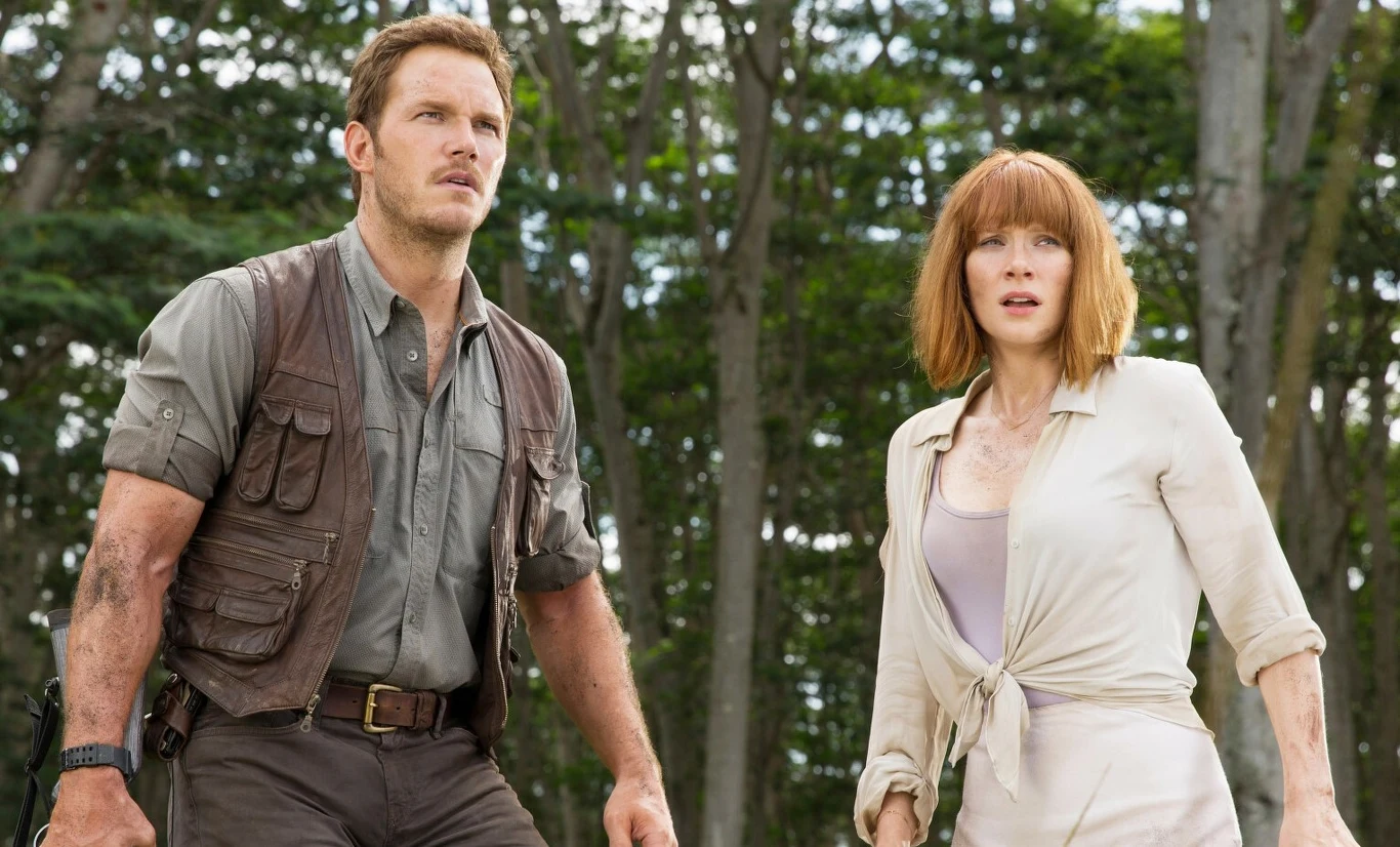 "Jurassic World" Kadr z filmu „Jurassic World”: dwoje ludzi w ubraniach terenowych stoi w lesie wśród drzew.
