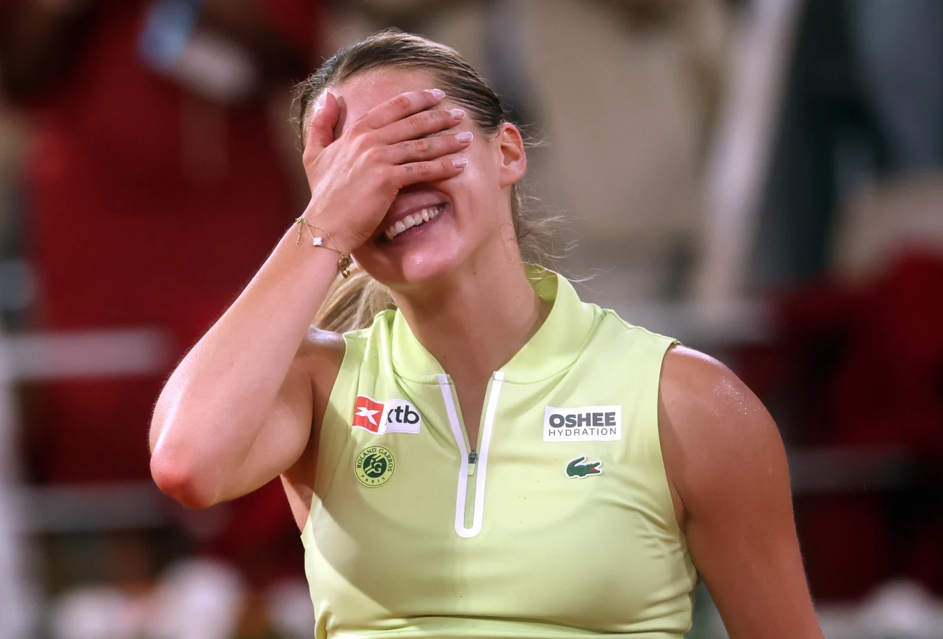 Uśmiechnięta kobieta w stroju sportowym zakrywa twarz dłonią, wyrażając silne emocje podczas wydarzenia sportowego.
