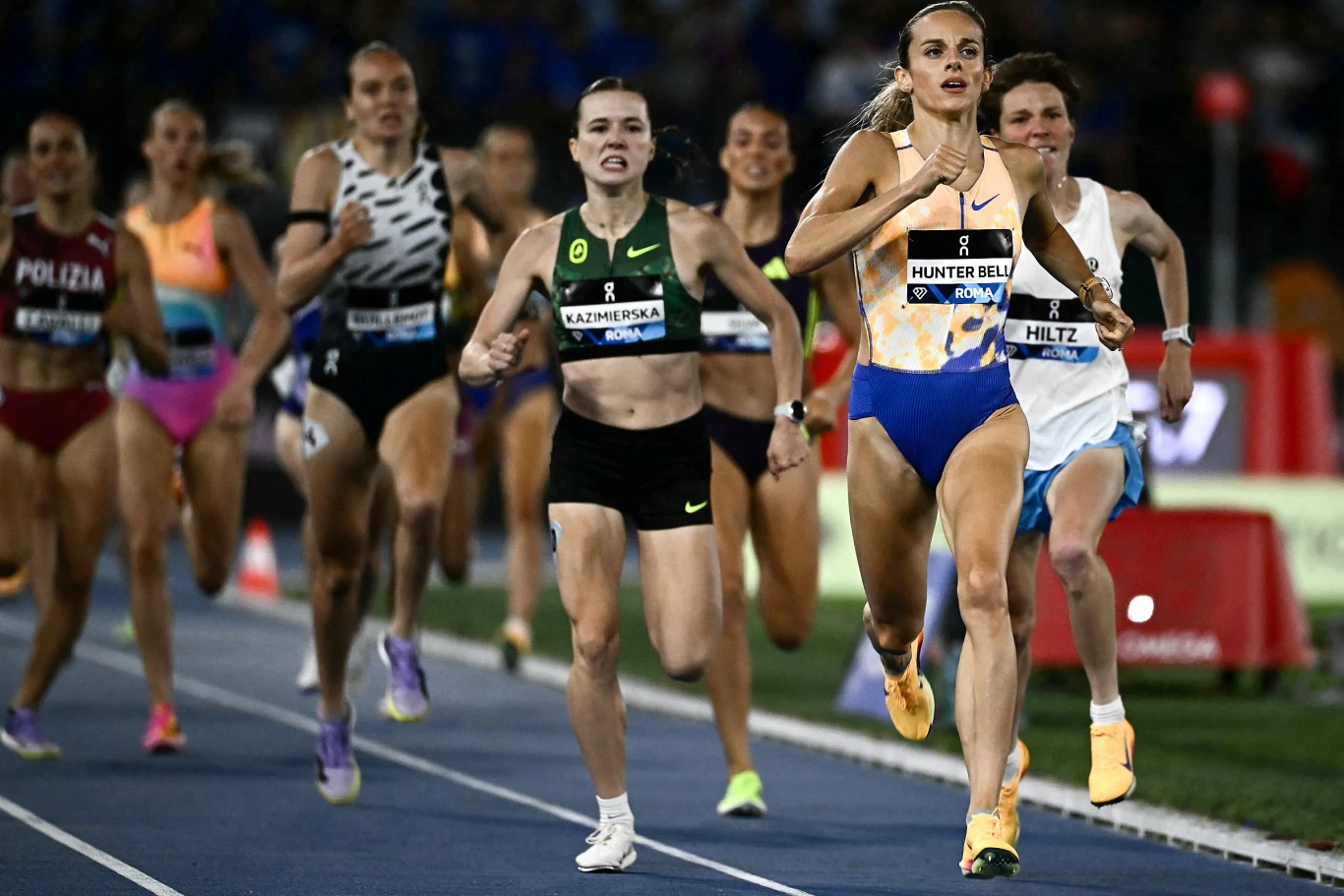 Georgia Hunter Bell finiszuje w Rzymie, za jej plecami walczą Klaudia Kazimierska i Nikki Hiltz Grupa zawodniczek biegnących po niebieskiej bieżni stadionu lekkoatletycznego podczas wyścigu na średnim dystansie, z wyraźnie prowadzącą biegaczką w żółto-niebieskim stroju.