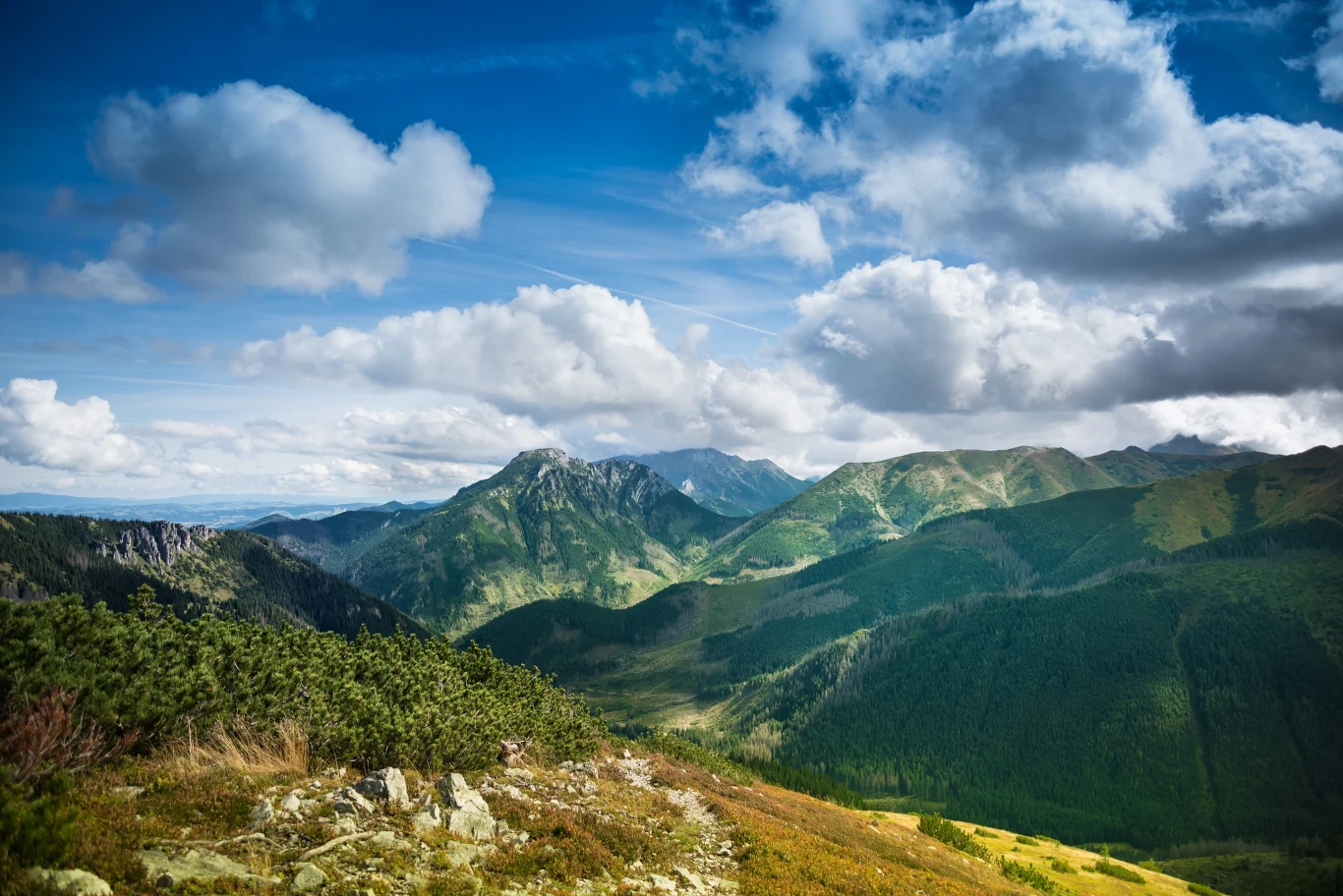 Gdzie warto jechać w Tatry zamiast do Zakopanego? Panorama Tatr z zielonymi szczytami, dolinami i dynamicznie ułożonymi chmurami na niebie.