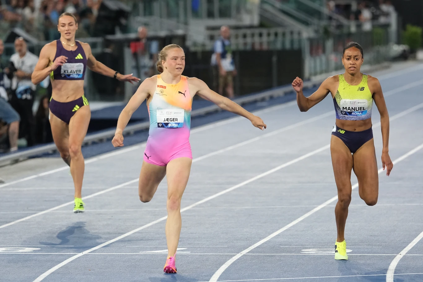 Trzy zawodniczki sprintują na bieżni lekkoatletycznej, wyraźnie walcząc o zwycięstwo tuż przed linią mety.
