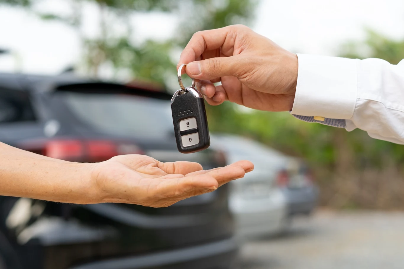 Dofinansowanie PFRON na auto 2026. Kto może otrzymać wsparcie? Przekazanie kluczyków samochodu na tle zaparkowanego auta w kontekście dofinansowania PFRON na 2026 rok.