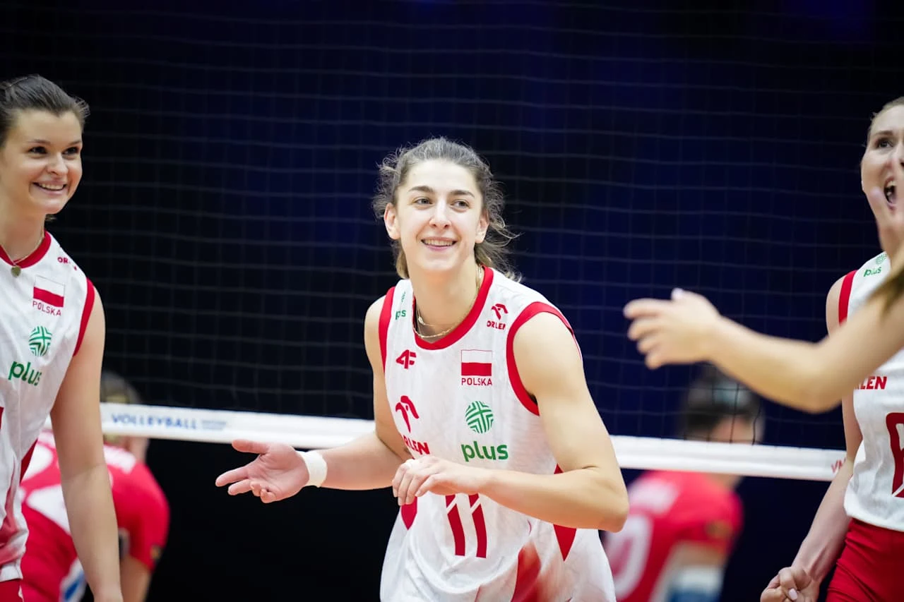 Szczęśliwe siatkarki w biało-czerwonych strojach z orzełkiem i logo sponsora świętujące punkt podczas meczu na hali sportowej.