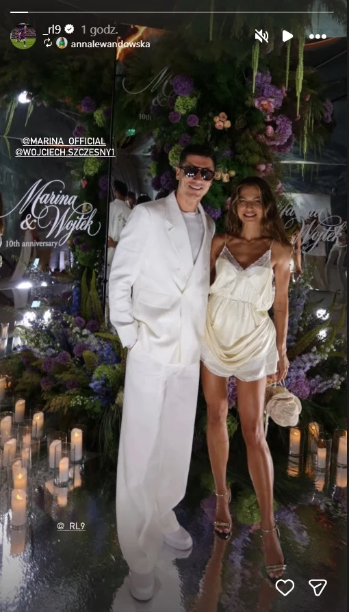 Elegancka para w jasnych stylizacjach pozuje na tle efektownej ściany udekorowanej kwiatami i zapalonymi świecami.