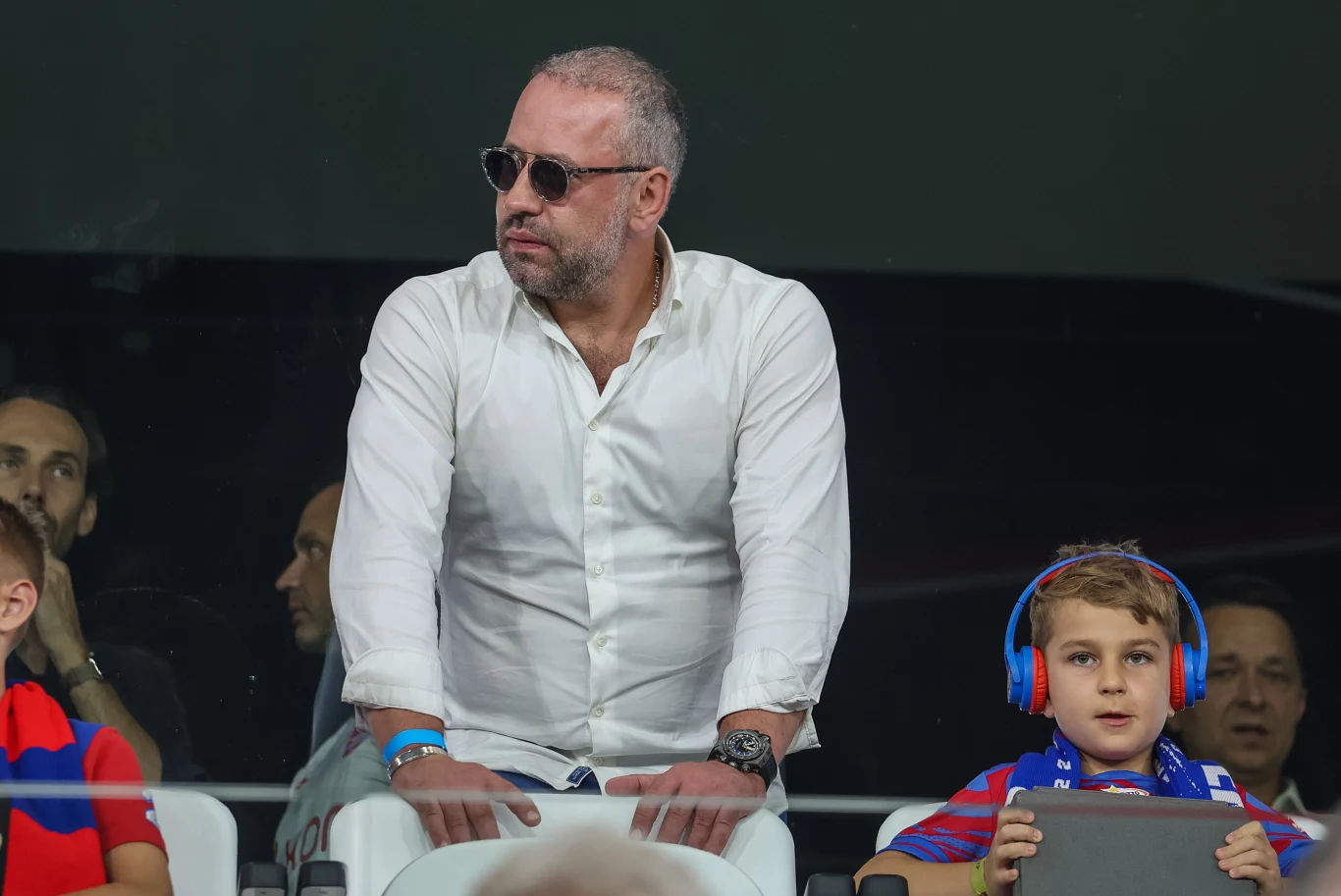 Bogusław Leśnodorski Bogusław Leśnodorski w białej koszuli i okularach przeciwsłonecznych obok chłopca ze słuchawkami i tabletem.
